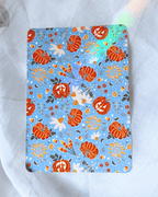 A light blue kindle insert decorated with a pattern of orange pumpkins, white flowers, and autumn leaves.
