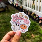 A sticker with a cartoon ghost, pumpkin, and the text 'Tis the Season'.