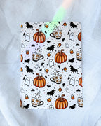 A kindle insert with a Halloween-themed pattern featuring orange pumpkins, black bats, white ghosts, and orange-and-white coffee cups, displayed on a white tulle fabric background with decorative fairy lights.