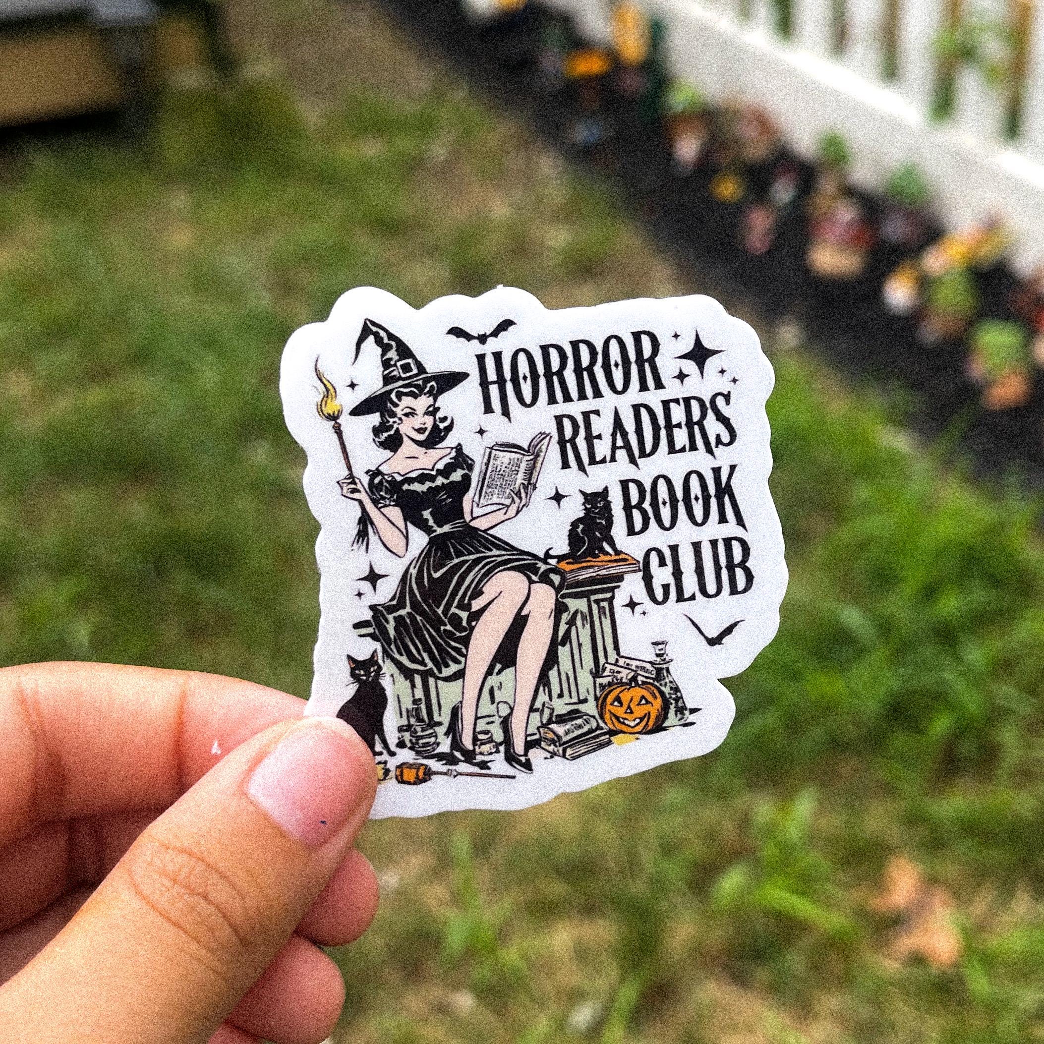 A witch reading a book with black cats, with the text "horror readers book club."