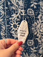 White marble acrylic motel keychain engraved with black sparkles and the lyrics "karma's a relaxing thought.'