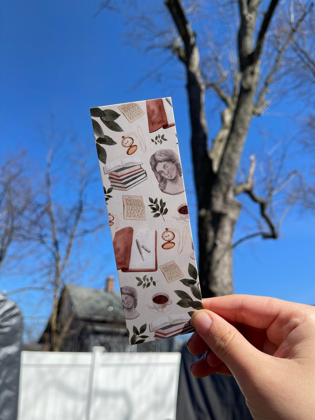 A bookmark with a light academic aesthetic design, featuring a mix of book-related imagery such as books, a camera, and decorative elements against a patterned background.
