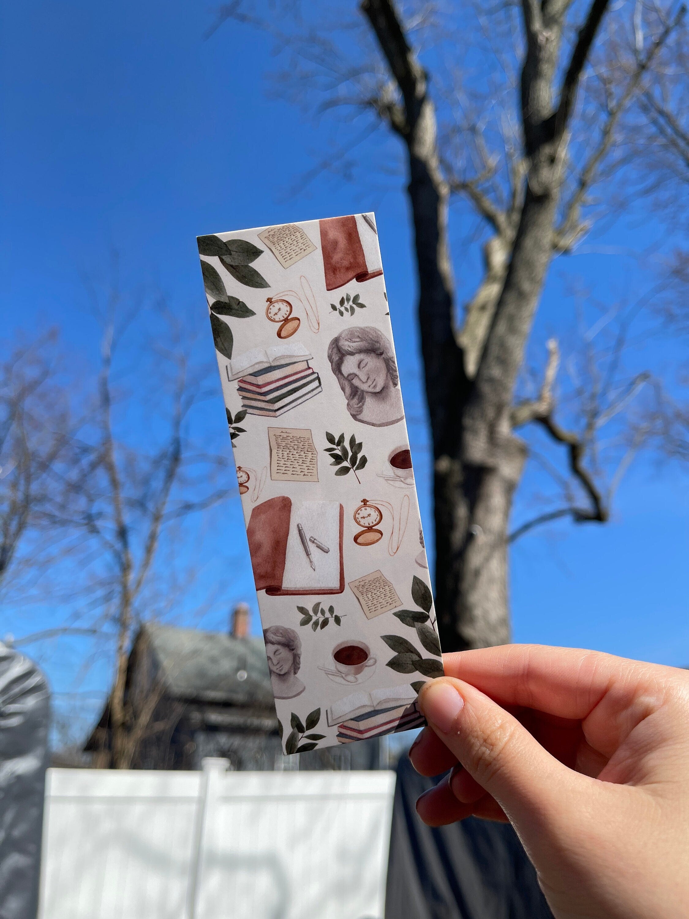A bookmark with a light academic aesthetic design, featuring a mix of book-related imagery such as books, a camera, and decorative elements against a patterned background.