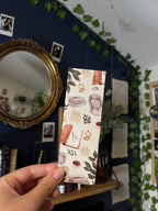 A bookmark with a light academic aesthetic design, featuring a mix of book-related imagery such as books, a camera, and decorative elements against a patterned background.
