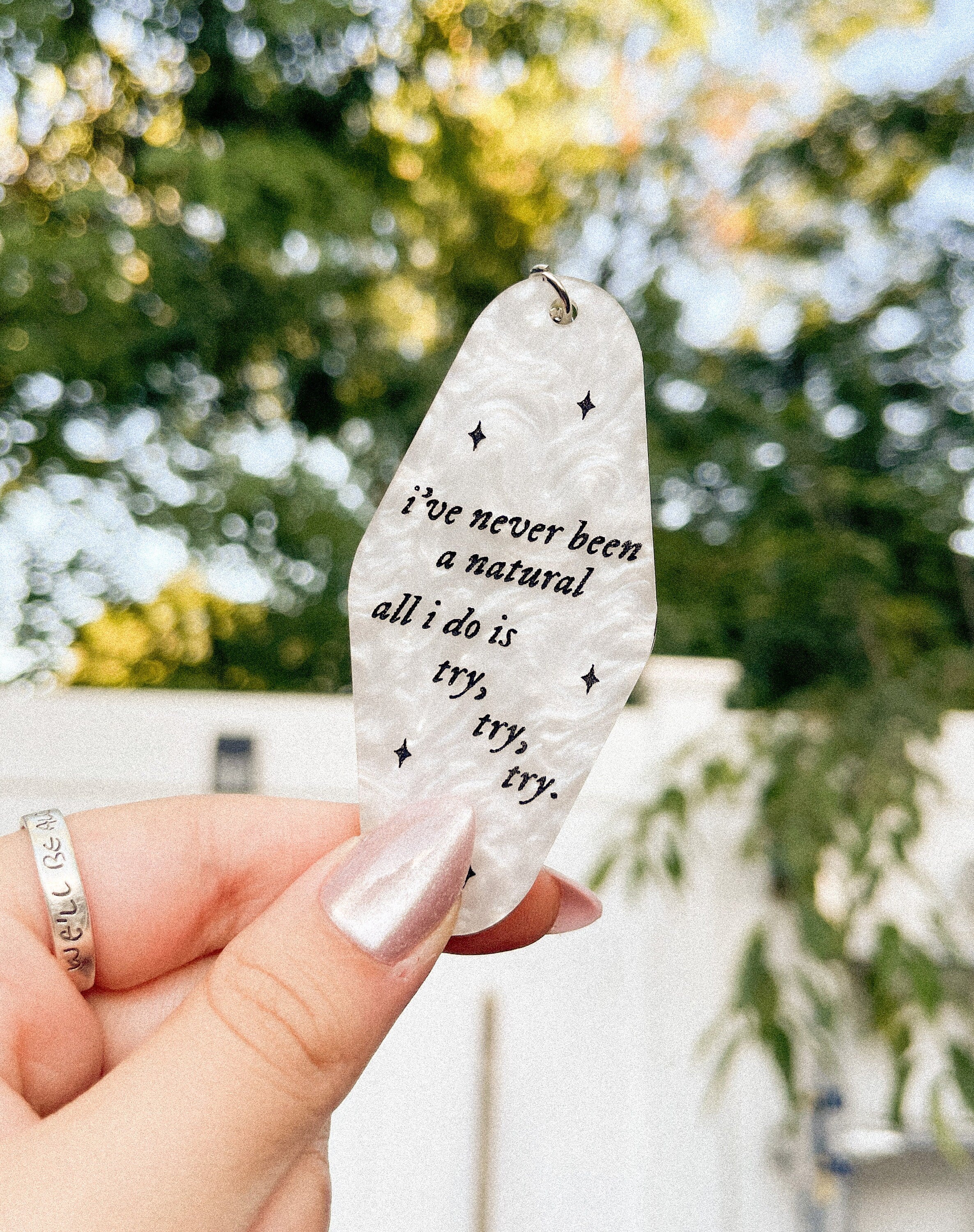 A white marble acrylic motel chain engraved with black sparkles and the text "i've never been a natural, all i do is try, try, try."