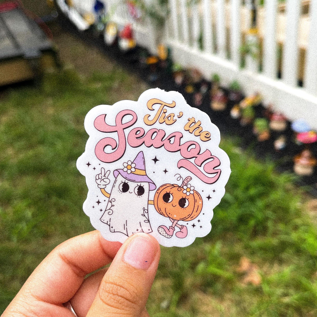 A sticker with a cartoon ghost, pumpkin, and the text 'Tis the Season'.