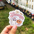 A sticker with a cartoon ghost, pumpkin, and the text 'Tis the Season'.