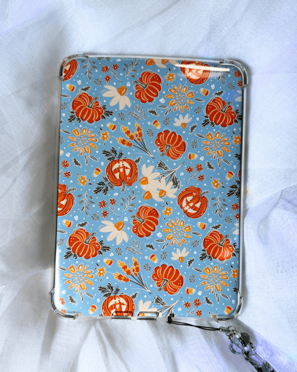 A light blue kindle insert decorated with a pattern of orange pumpkins, white flowers, and autumn leaves.