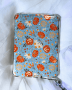 A light blue kindle insert decorated with a pattern of orange pumpkins, white flowers, and autumn leaves.