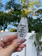 A hand holding a white marble-colored keychain with the text 'THE ROAD NOT TAKEN LOOKS REAL GOOD NOW' engraved on it inspired by taylor swift.