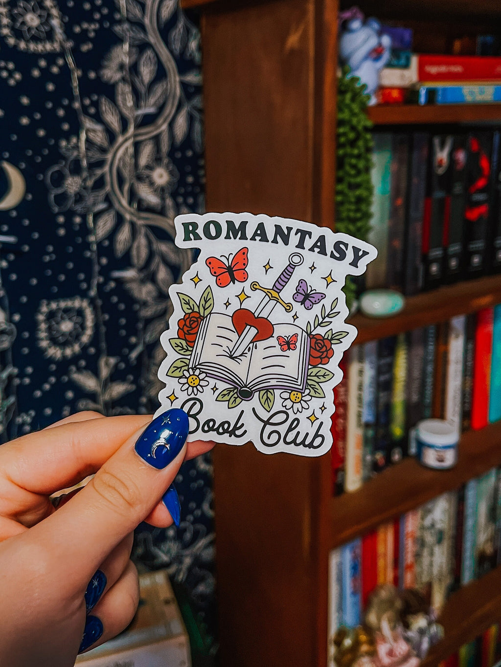 A transparent sticker with a book, butterfly, sword, and rose design, with the text 'Romantasy Book Club'.