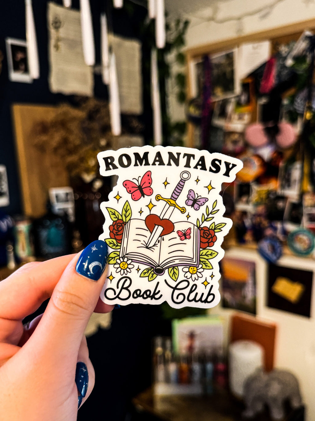 A transparent sticker with a book, butterfly, sword, and rose design, with the text 'Romantasy Book Club'.