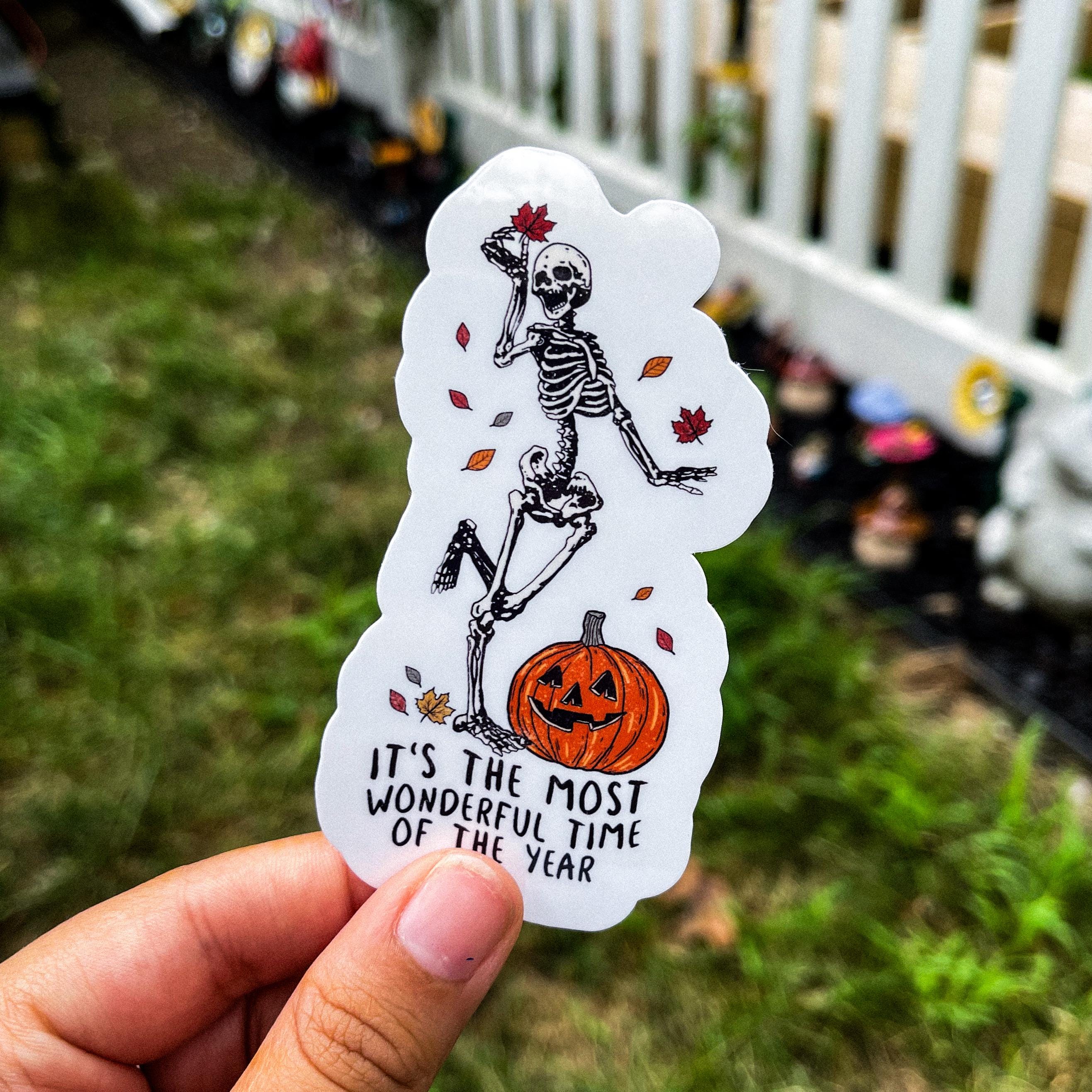 A sticker with a skeleton character, pumpkin, and autumn leaves with the text 'It's the most wonderful time of the year'.