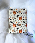 A kindle insert with a Halloween-themed pattern featuring orange pumpkins, black bats, white ghosts, and orange-and-white coffee cups.
