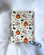A kindle insert with a Halloween-themed pattern featuring orange pumpkins, black bats, white ghosts, and orange-and-white coffee cups.