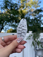 A hand holding a white marble acrylic motel keychain engraved with black sparkles and the text "if you never bleed you're never gonna grow"