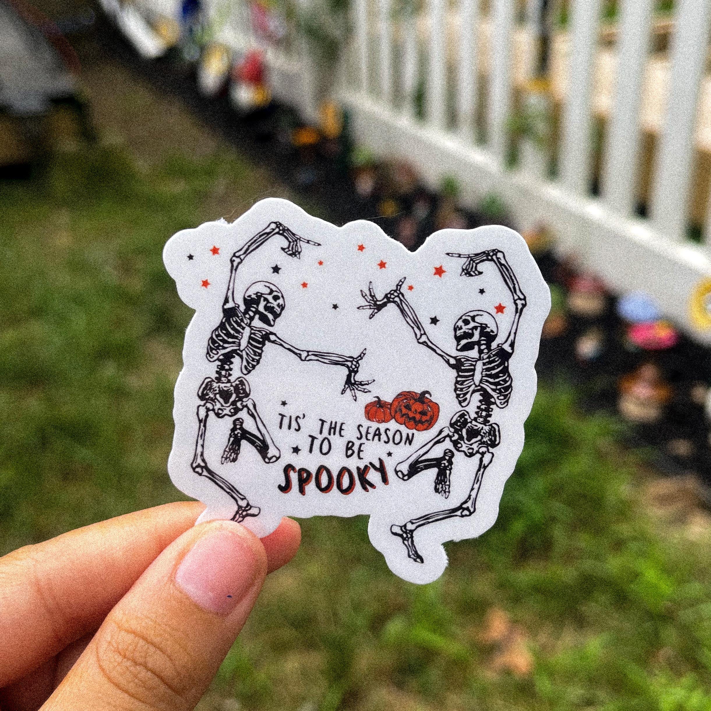 A sticker with a cartoon illustration of two skeletons dancing and the text 'IT'S THE SEASON TO BE SPOOKY'.