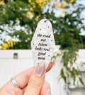 A hand holding a white marble-colored keychain with the text 'THE ROAD NOT TAKEN LOOKS REAL GOOD NOW' engraved on it inspired by taylor swift.
