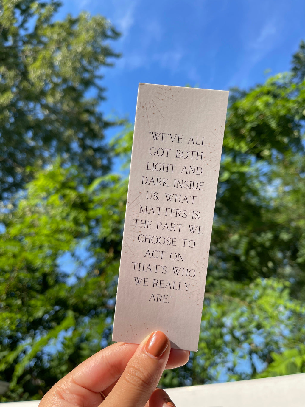 A hand holding a white bookmark with a quote by Sirius Black from the Harry Potter series. "We've all got both light and dark inside us. What matters is the part we choose to act on. That's who we really are."
