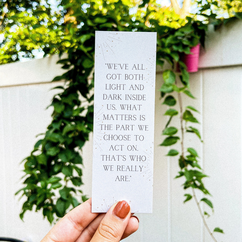 A hand holding a white bookmark with a quote by Sirius Black from the Harry Potter series. "We've all got both light and dark inside us. What matters is the part we choose to act on. That's who we really are."